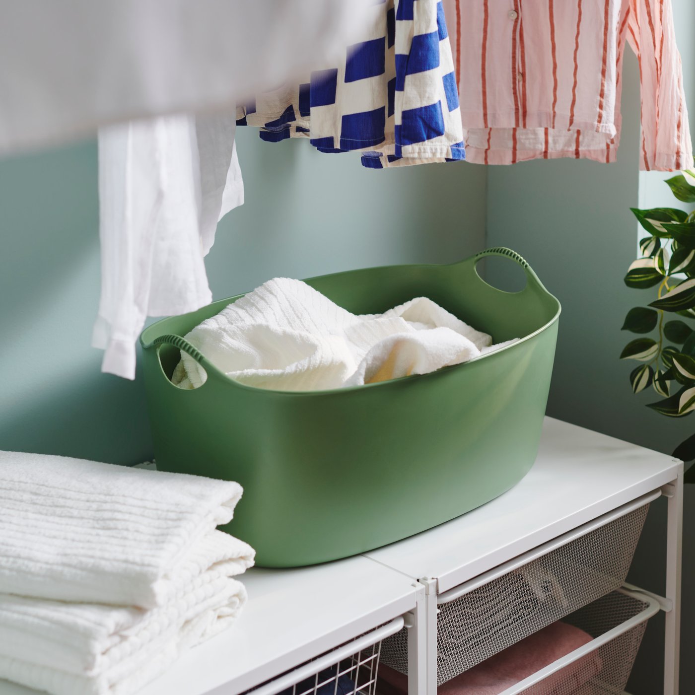 A 35-liter green, indoor/outdoor TORKIS flexi laundry basket holds towels on a white surface where clean towels are stacked.