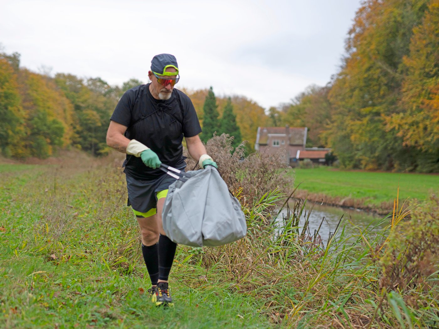 A man jogging in the nature while picking up trash and putting it in a AJÖSS waste bag.