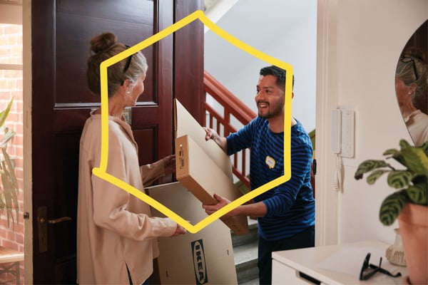 En kvinde tager imod en levering af flatpacks fra IKEA af en mand i en entre.