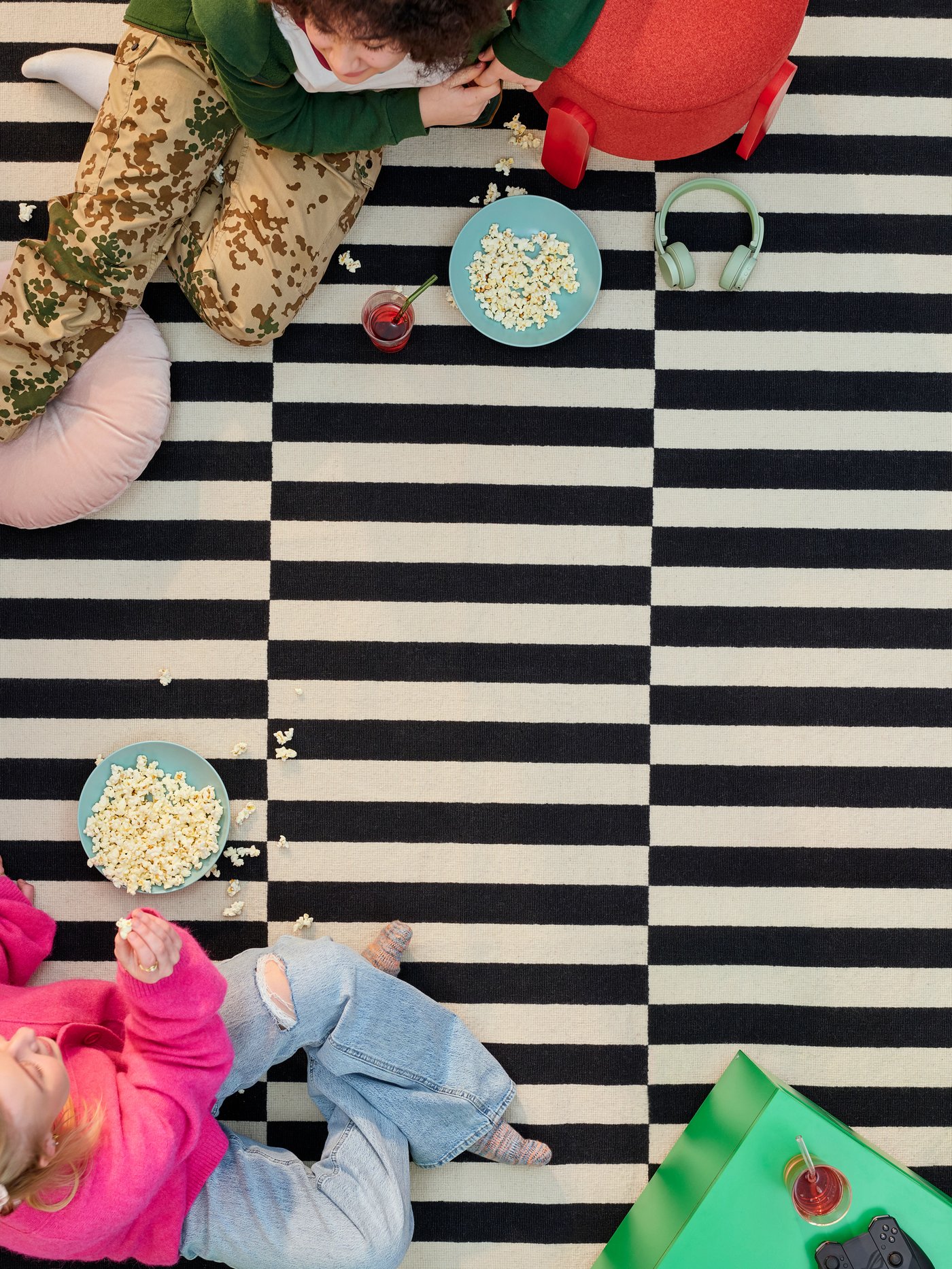 A black-and-white striped STOCKHOLM rug with two people sitting on it, each holding a bowl of popcorn.