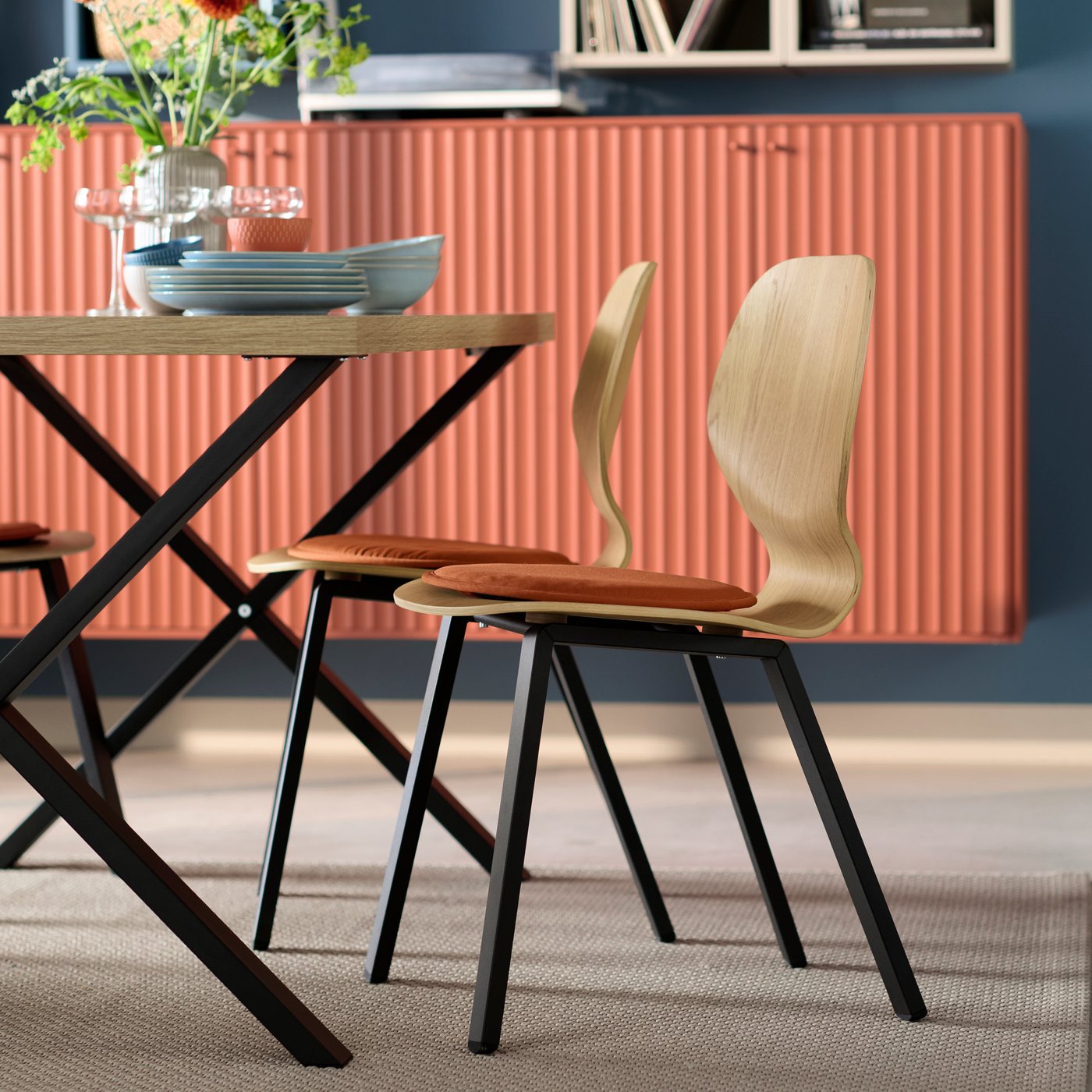 Two SKÅLSTA chairs with seat shells in oak veneer and black legs are placed next to a SKÅLSTA table in matching colours.