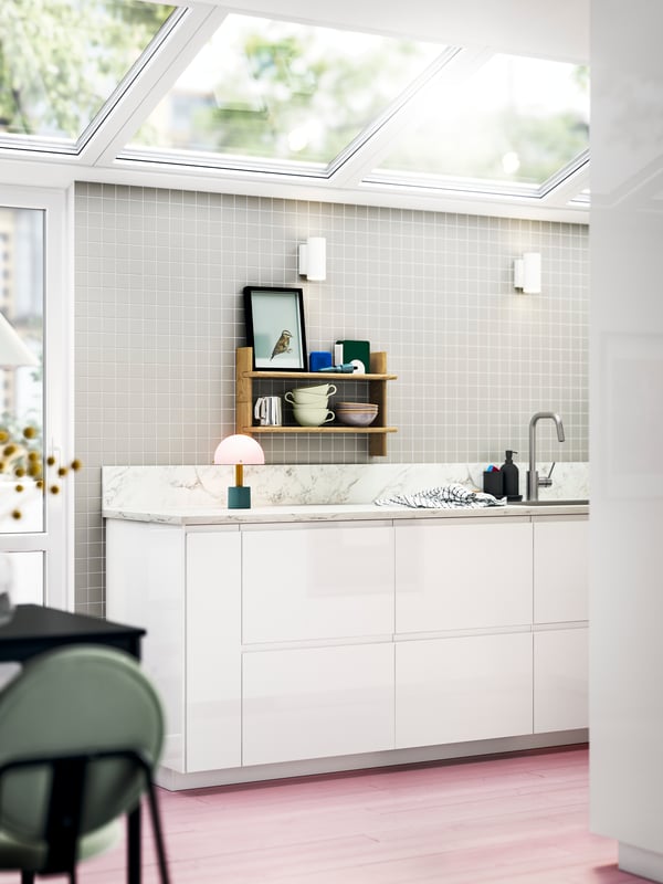 A light-filled kitchen with VOXTORP high-gloss white fronts and open shelves featuring bowls and colourful decor.