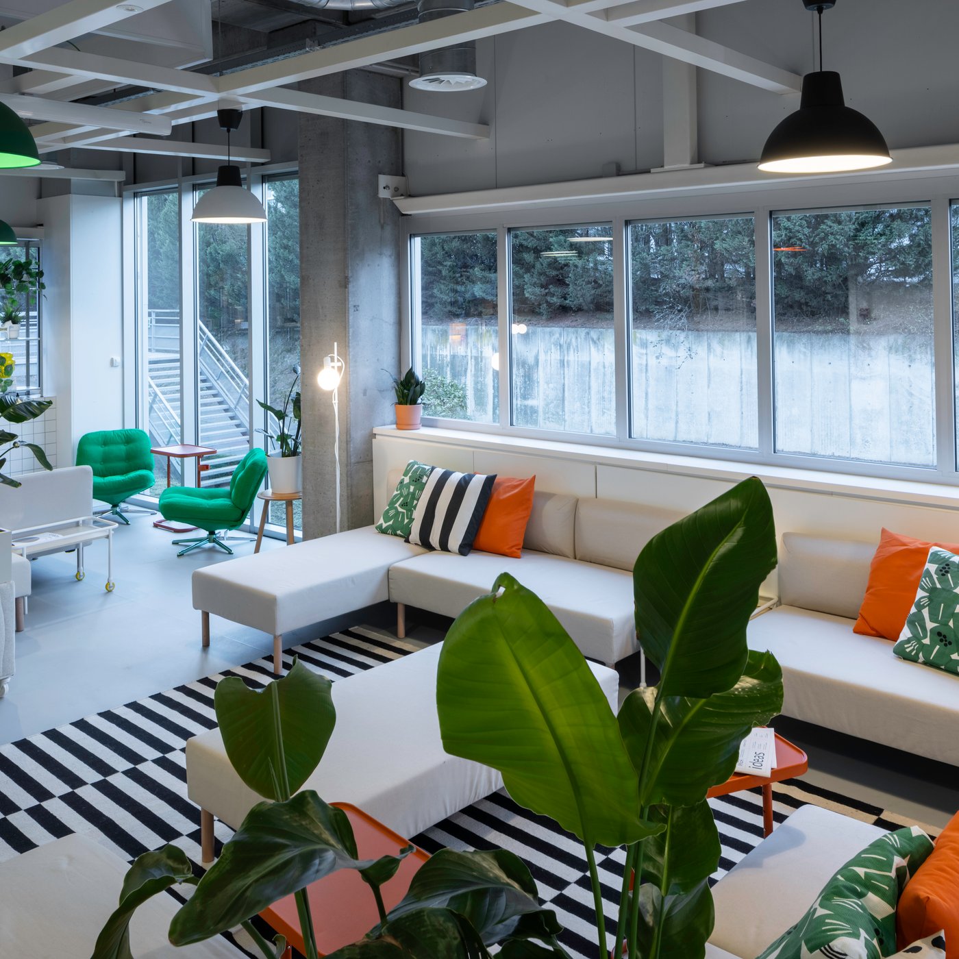 Un salon lumineux avec des assises IKEA, des coussins ludiques et beaucoup de verdure crée une atmosphère fraîche et accueillante, idéale pour une courte pause ou une conversation informelle.