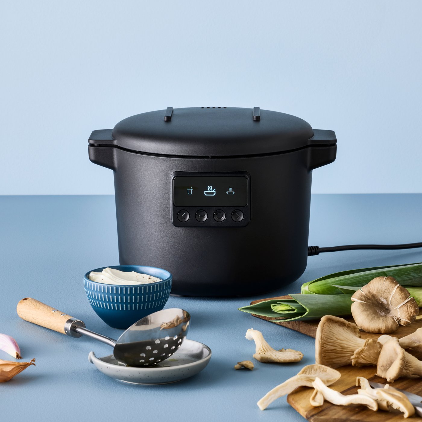 A TILLREDA multicooker standing on a countertop together with ingredients and kitchen utensils.
