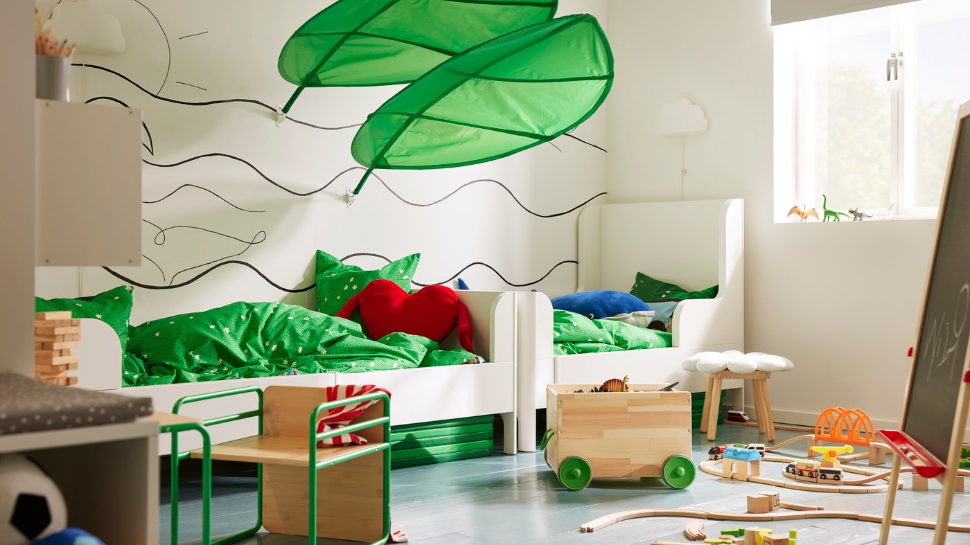 A children’s room with two white beds along a wall with waves painted on it, LÖVA bed canopy over the beds, toys everywhere.