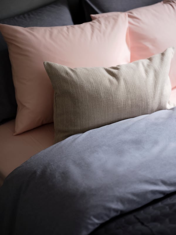 Le dessus d’un lit avec plein de coussins avec taies d'oreiller DVALA rose clair et des draps de lit KOPPARBLAD bleu foncé.