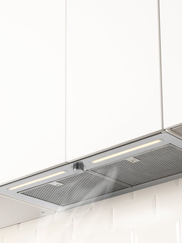 A close-up of a built-in in extractor hood placed under a white cabinet, sucking air above the worktop.