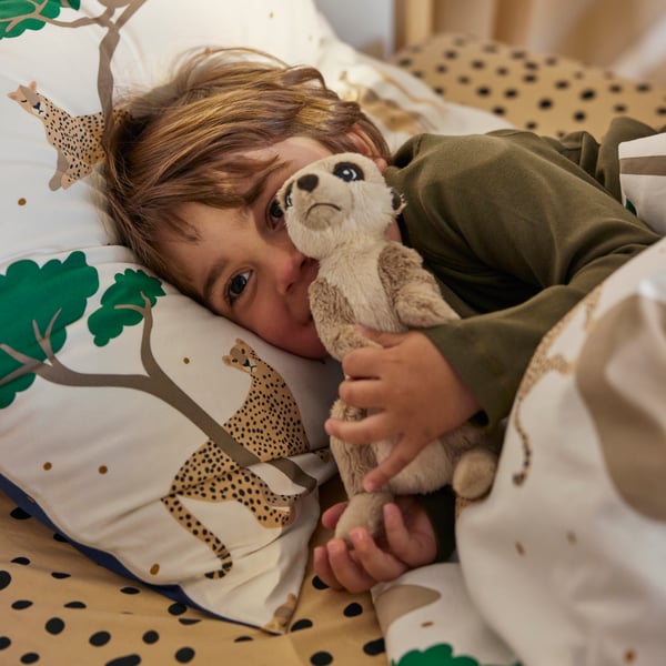 A child is cuddling with a soft toy meerkat in a bed with a white/dark blue SANDLÖPARE duvet cover and pillowcase.