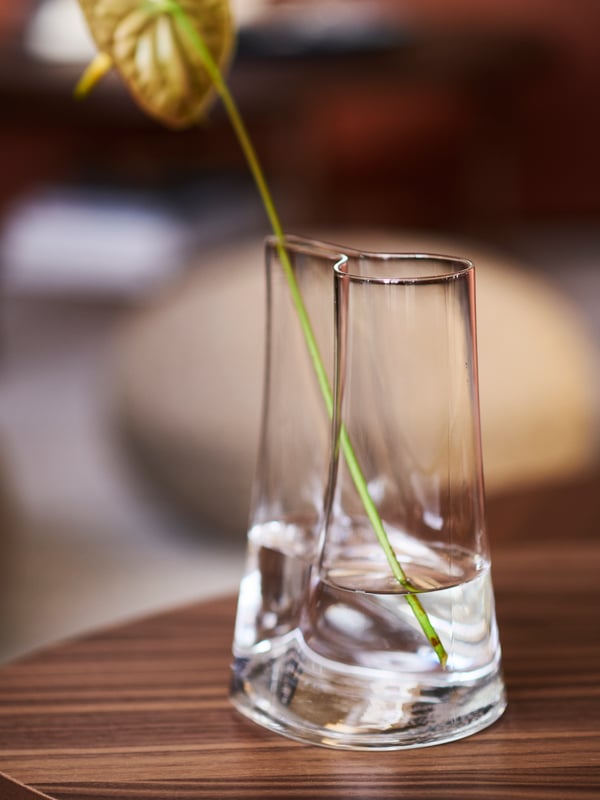 Un vase en verre CHILIFRUKT autour d’une surface ronde en bois brun avec un peu d'eau et une fleur dedans.