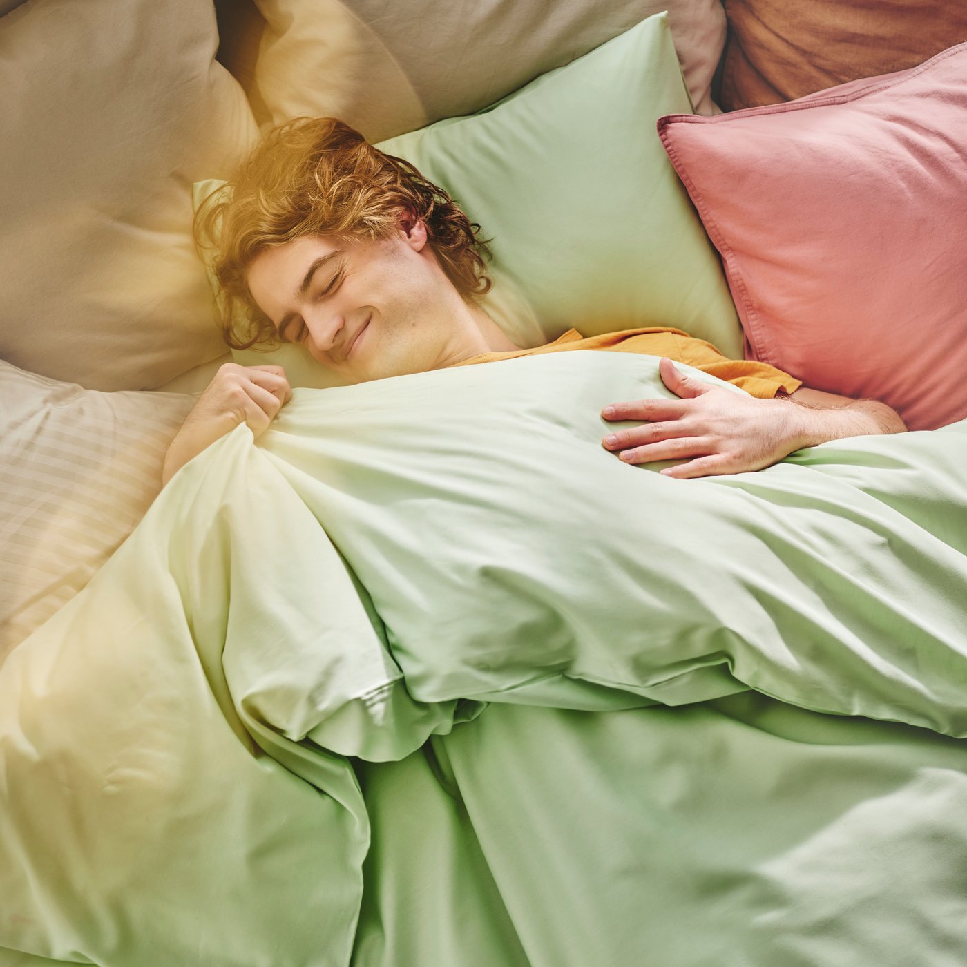 A person is lying in bed under a green ÄNGSLILJA duvet cover with a pink pillowcase.
