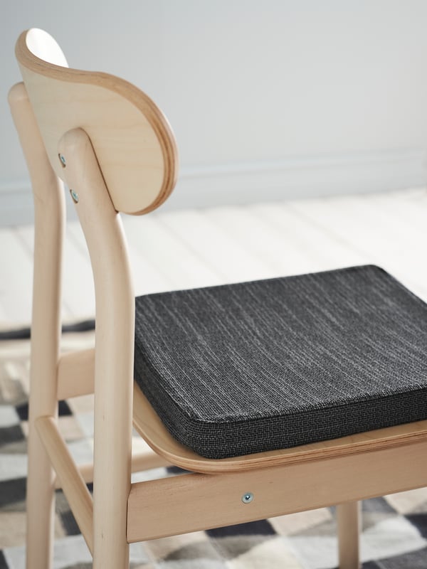 A white LIDÅS dining chair next to a dining table. Attached to the chair is RAGGARV neck-lumbar pillow.