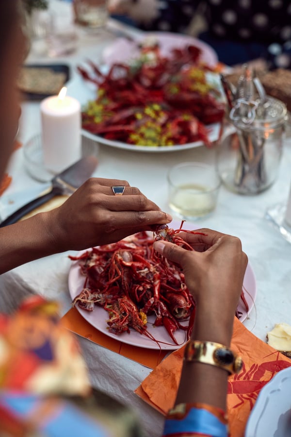 A person eating a crayfish, with other plates of crayfish pictured in the background.