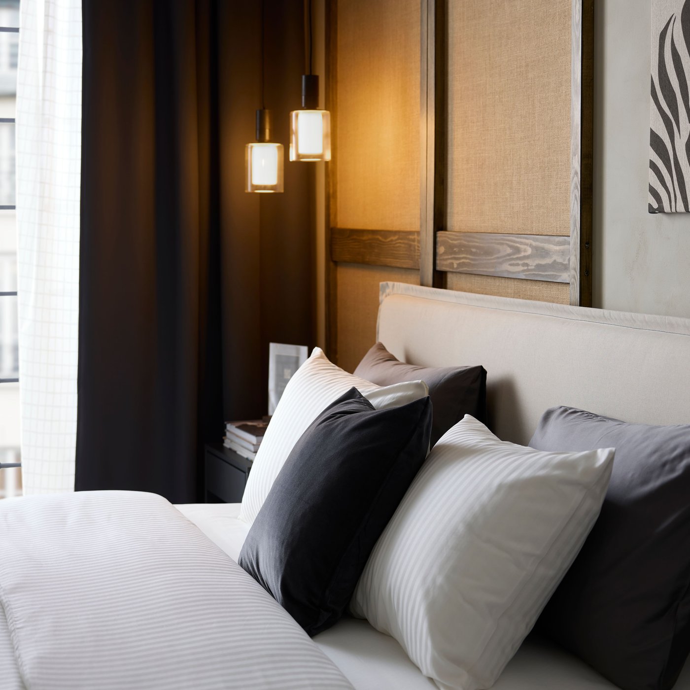 Ein Hotelbett ist mit Reihen von Kissen sowie einem dezent gestreiften, weiß glänzenden NATTJASMIN Satin-Bettbezug und passenden Kissenbezügen ausgestattet.