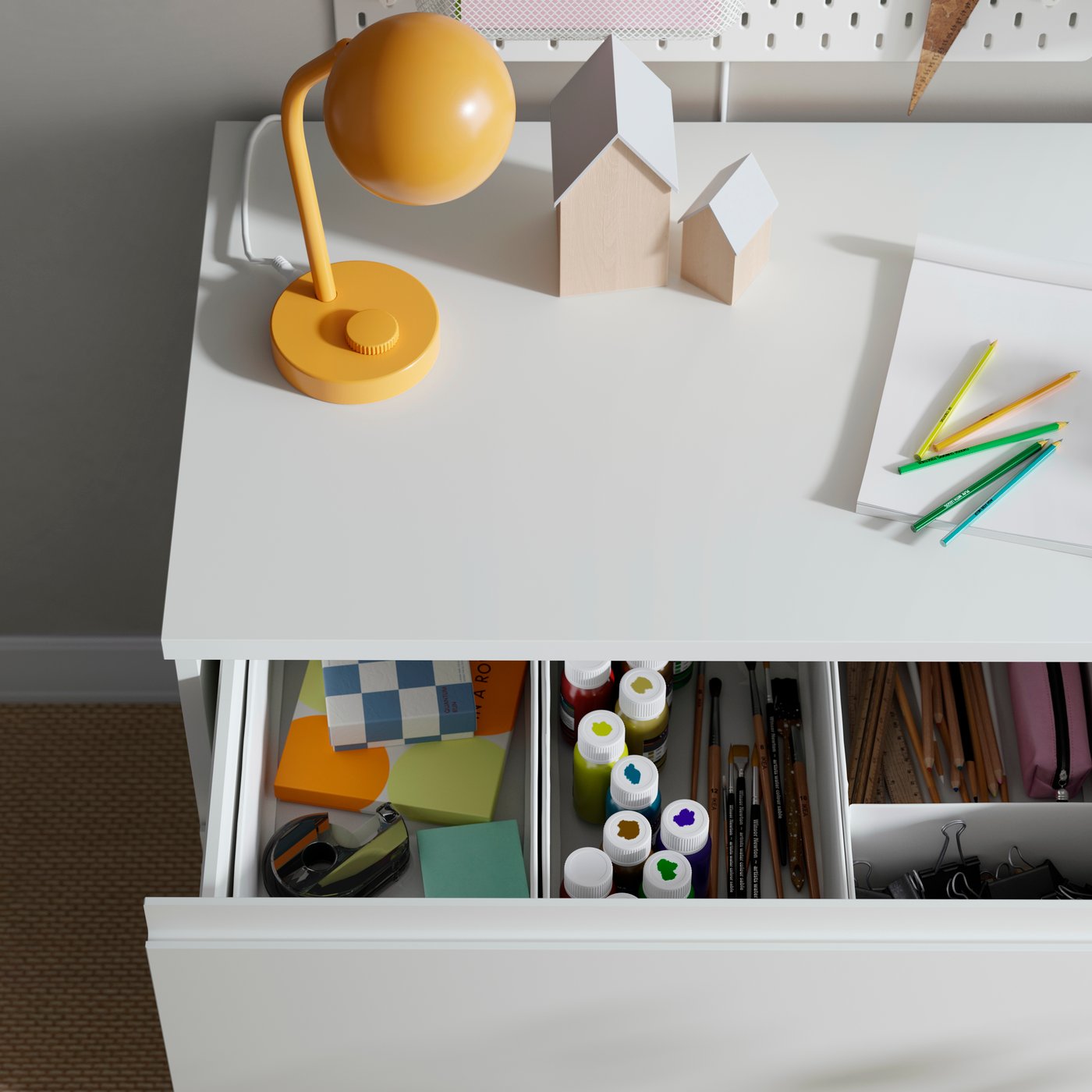 Vista superior de un cajón abierto de una cómoda STORKLINTA blanca de tres cajones, lleno de materiales para manualidades.