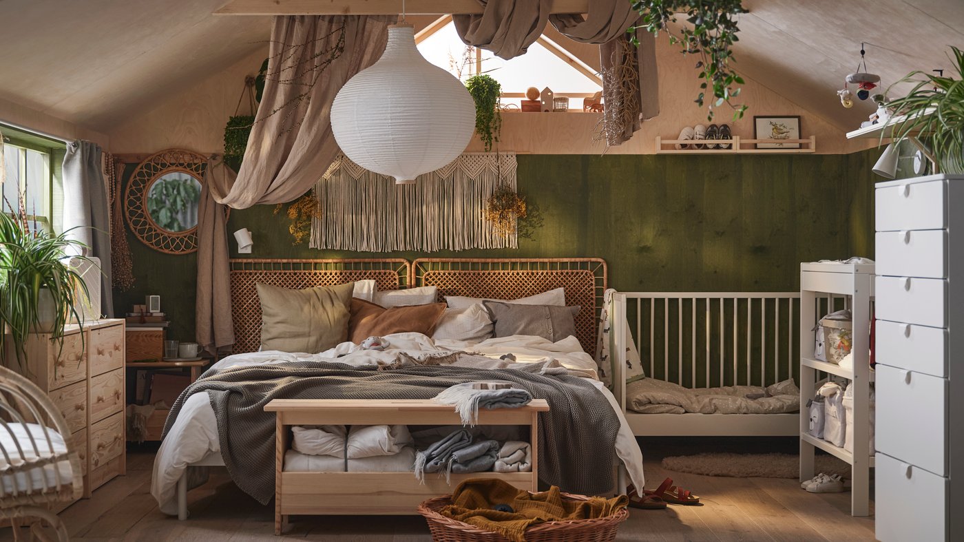 Chambre dans le style boho avec un lit double revêtu de linge de lit et de coussins dans des tons neutres, à côté d’un lit bébé GULLIVER blanc.