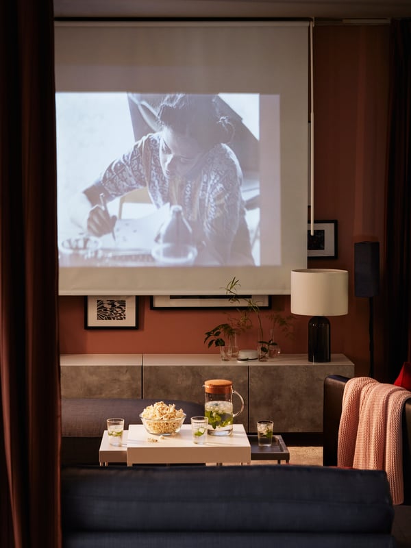 Film en cours de projection au salon sur un store occultant à enrouleur, banc TV avec portes, popcorn.
