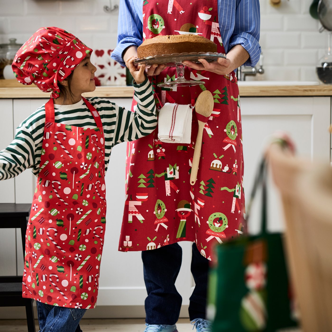 Debout dans une cuisine, enfant et adulte portant des tabliers VINTERFINT assortis et ornés d’un motif festif.
