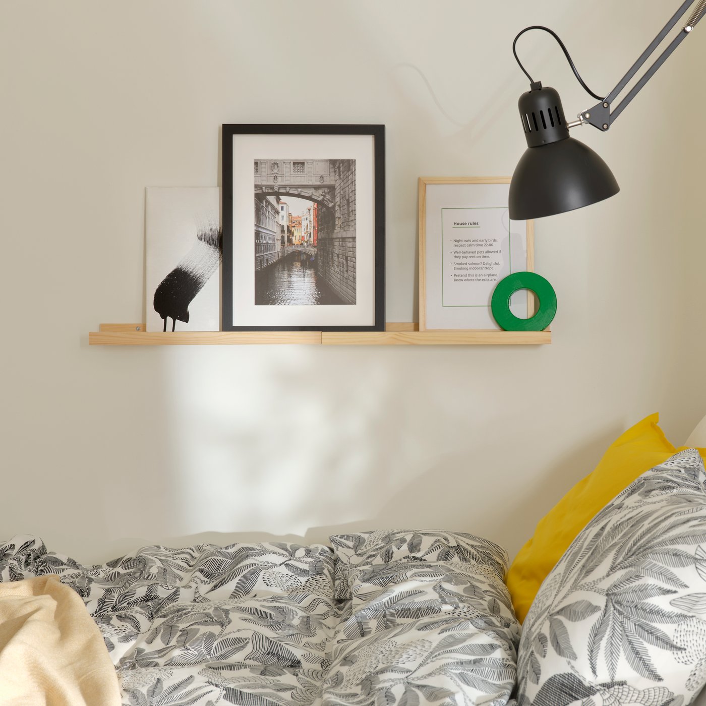 Two pine NORDHÄGG picture ledges are on  a wall above a bed,  holding a framed list of house rules and other artwork.