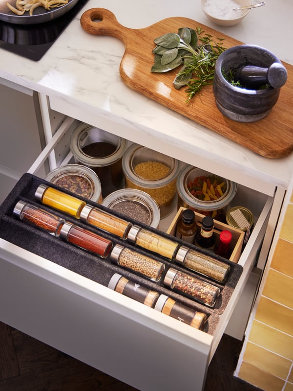 An open drawer with an UPPDATERA sliding organiser with diverse items, on top is an ÄDELSTEN pestle/mortar in marble black.