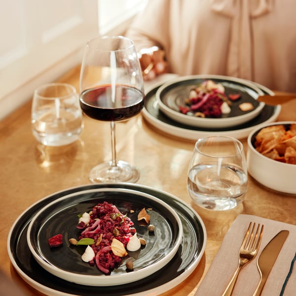 Green plates with colourful salads served on them are placed on a light brown table with DYRGRIP glasses for wine and water.