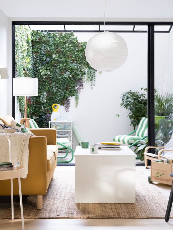 Dans un salon, une suspension REGOLIT pend au-dessus d’une table basse réglable ÖSTAVALL blanche, à côté d’un canapé PÄRUP jaune-brun.