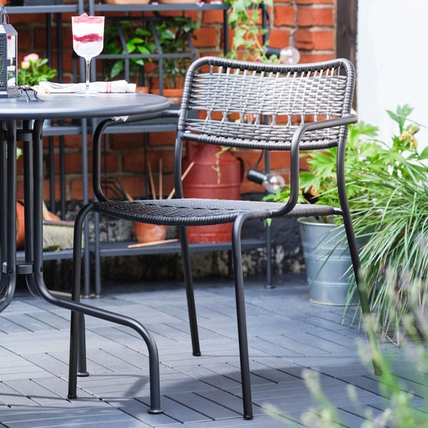 Una silla de terraza LÄCKÖ en un espacio con plantas y un estante con maceteros y plantas.