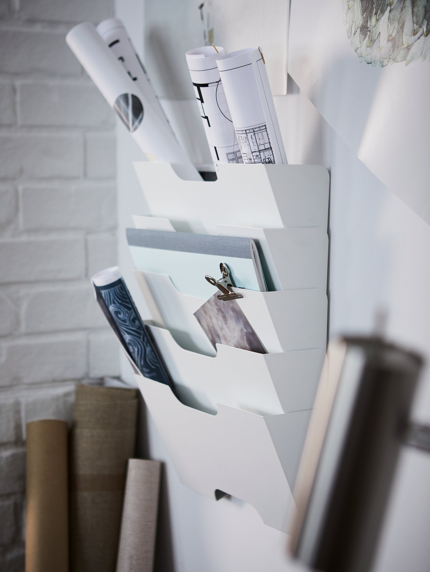 A white KVISSLE wall newspaper rack keeping documents and drawings in order. Cardboard rolls are leaning against the wall.