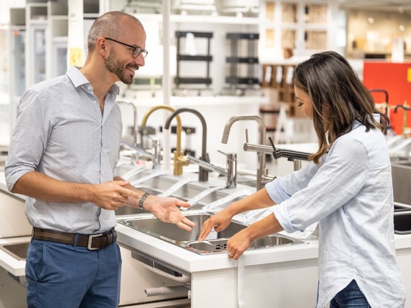 Two people with blue shirts talking and measuring a ceramic cooktop while they are talking.