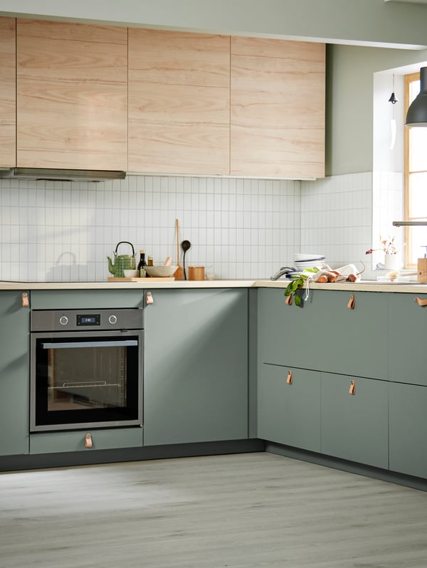 Una cocina luminosa y espaciosa combina puertas ASKERSUND con efecto fresno claro en los muebles altos y frentes de color gris verdoso en los muebles bajos.