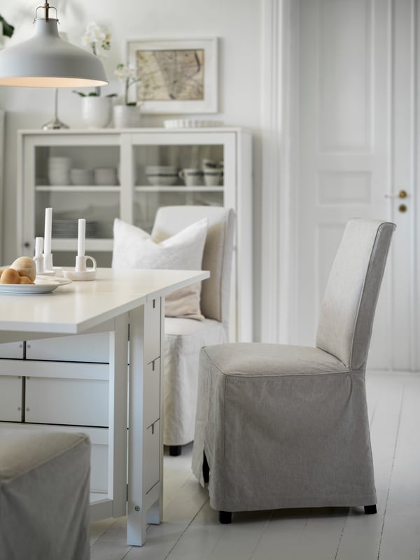 A BERGMUND chair with a long white cover stands in front of a dining table.