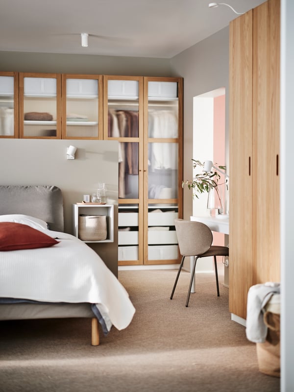 A SAGESUND upholstered bed in Diseröd brown/Luröy in a bedroom in front of a TONSTAD/PAX wardrobe in white/oak veneer/glass.