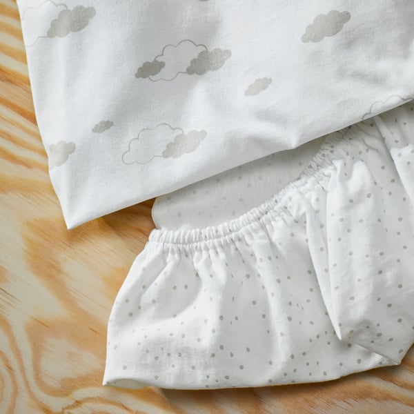 Deux draps housses ÄLSKVÄRD pour berceau, l’un à pois et l’autre à nuages, sur une surface en bois.