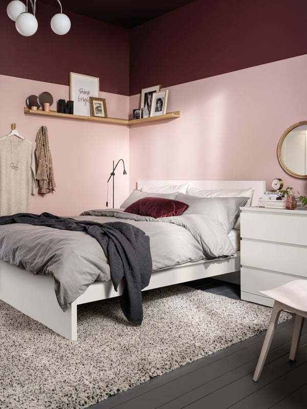 A white MALM bed on a white VINDUM high pile rug in a pink and dark red room. The bed has grey ÄNGSLILJA bed linen on it.