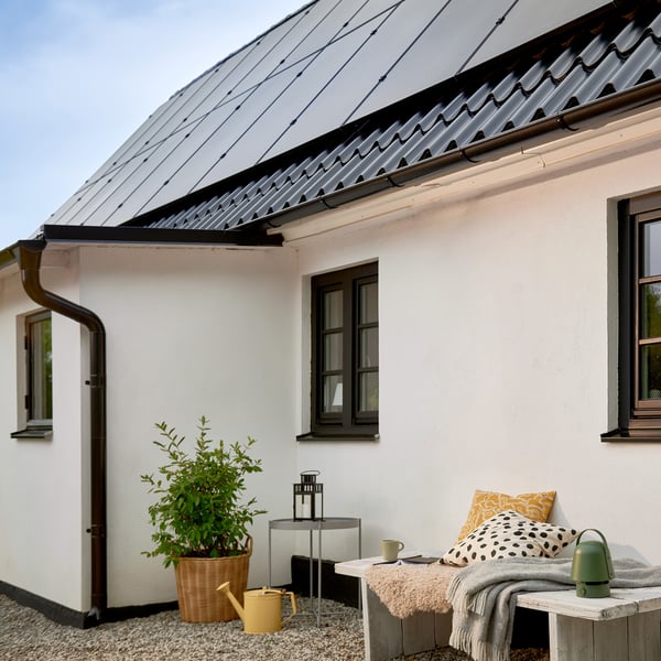 Seitenansicht eines grossen weissen Hauses mit einem Dach, das mit Sonnenkollektoren ausgestattet ist.
Eine schwarze/aussenliegende SVARTRÅ LED-Lichterkette mit 20 Glühbirnen vor einem Haus mit Sonnenkollektoren auf dem Dach.