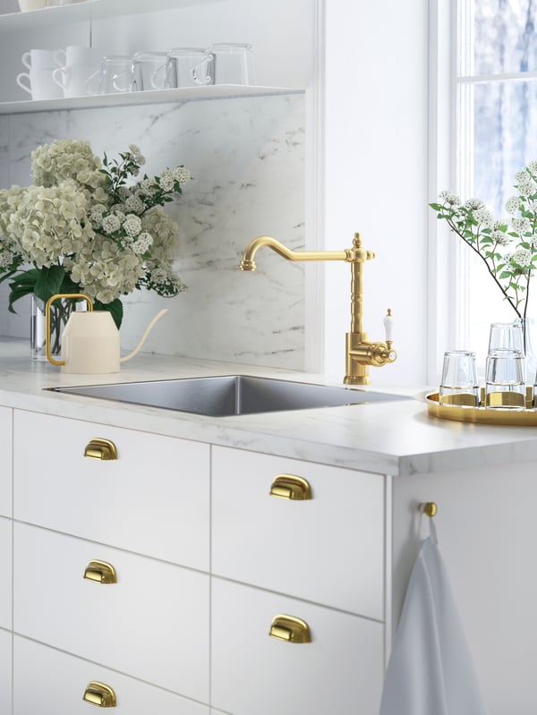 A kitchen with EKBACKEN white marble effect/laminate worktop, white fronts and brass-coloured tap and handles.