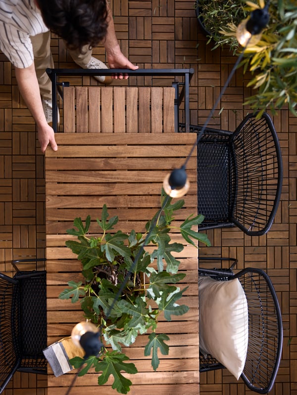A potted plant on a VÄSMAN extendable outdoor table surrounded by anthracite TALLSKÄR outdoor chairs with armrests.