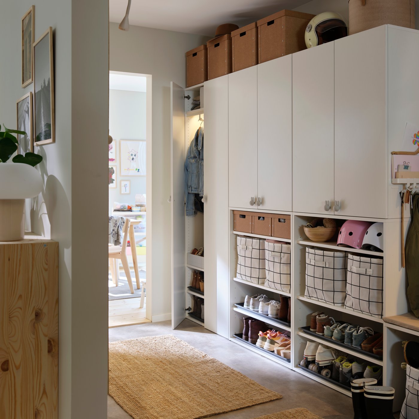 A well-organized hallway featuring a large white storage unit with cabinets, open shelves filled with bins and baskets, and shoe racks. A woven rug is on the floor.