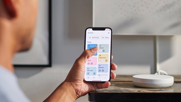 Žena koja drži pametni telefon koristi aplikaciju IKEA Home smart, kojom kontroliše svetlost lampi