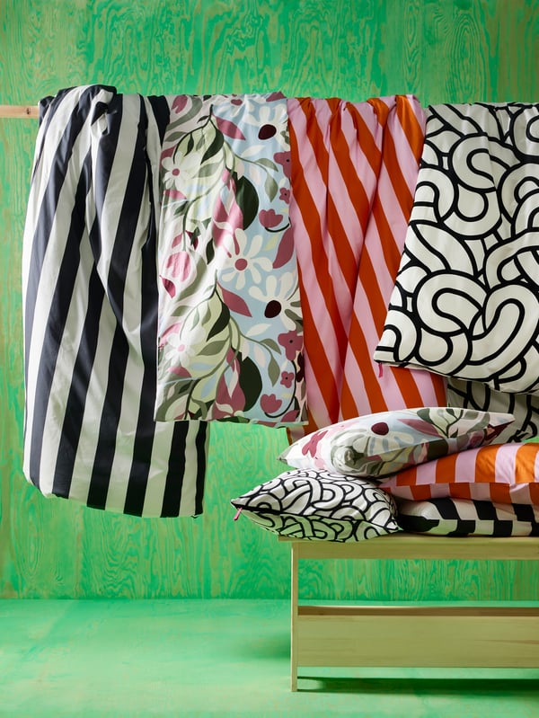 Duvet covers and cushions from SÖTRÖNN collection in various patterns and colours hanging in front of a bright green background. 