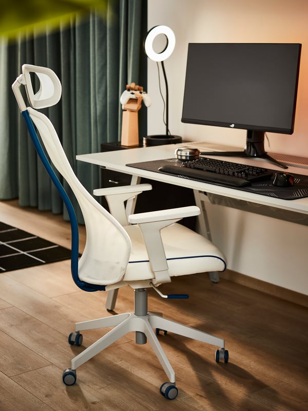 A Bomstad white MATCHSPEL gaming chair standing on a wooden floor with green-blue HANNALENA room darkening curtains behind.