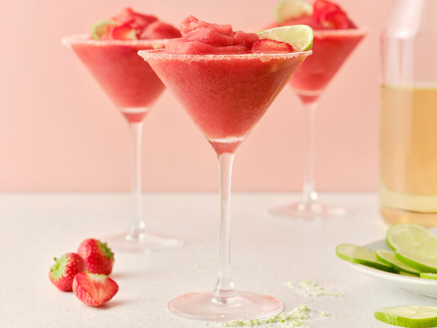 Three tall glasses filled with margaritas made with ISKUB elderflower soda and frozen strawberries, garnished with lime slices.