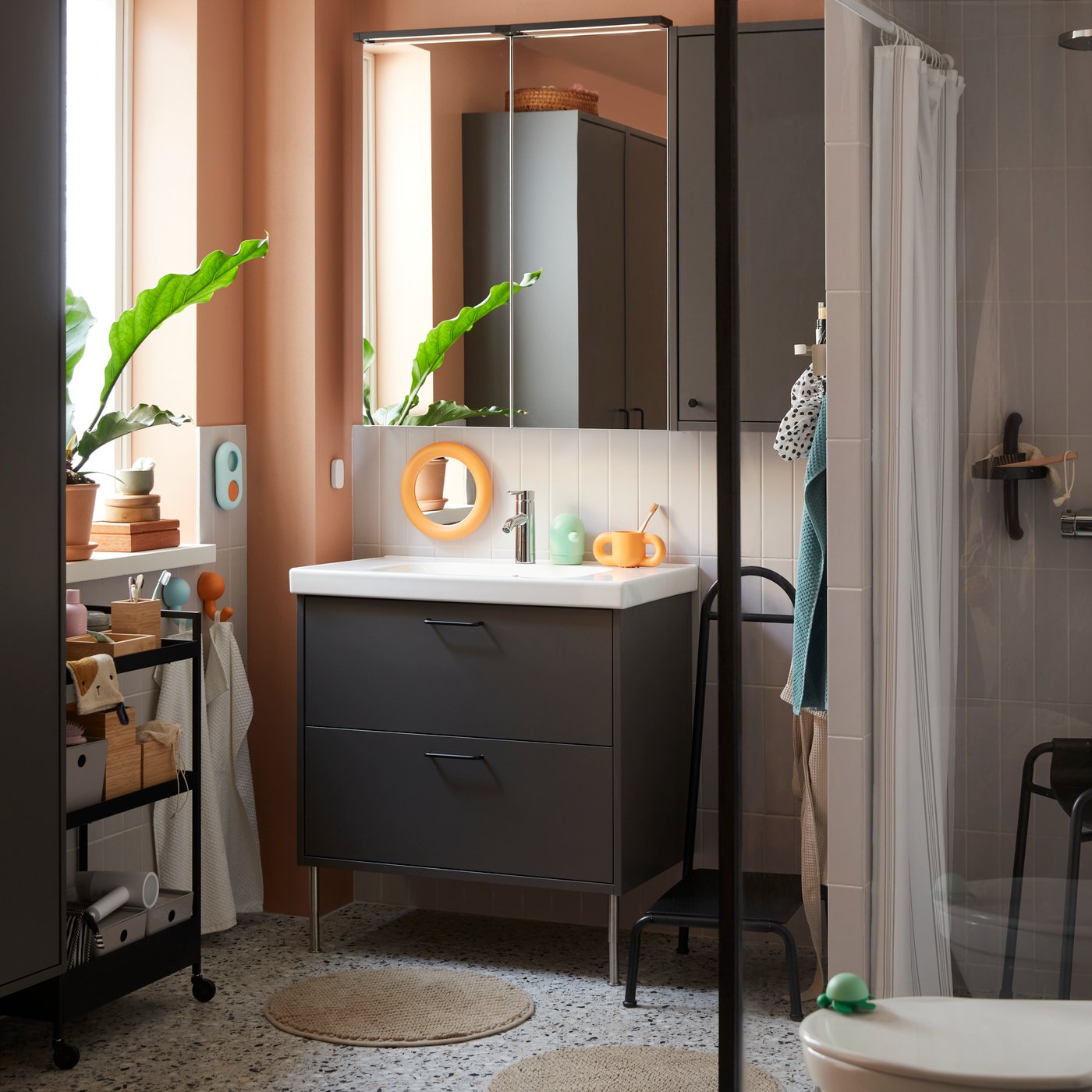 Ein Badezimmer mit einem dunkelgrauen HAVBÄCK Waschtisch mit Schubladen, Waschbecken und Wasserhahn, dazu Spiegel und Badezimmerausstattung.