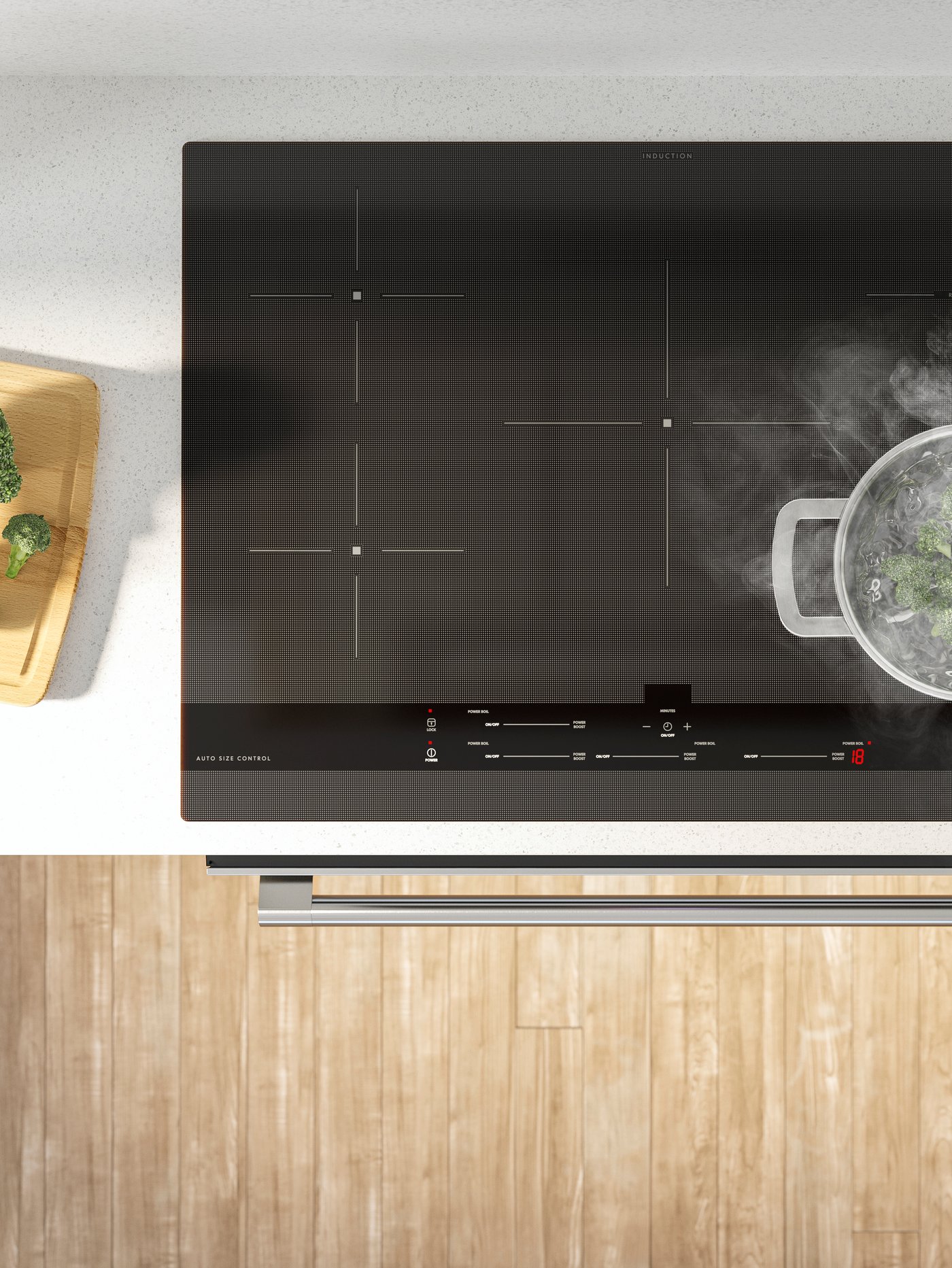 Viewed directly from above, an induction hob with a silver pot boiling vegetables, on a white worktop.
