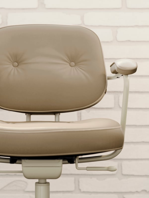 The thick, padded leather seat and back of a beige ALEFJÄLL office chair, placed in front of a white brick wall.