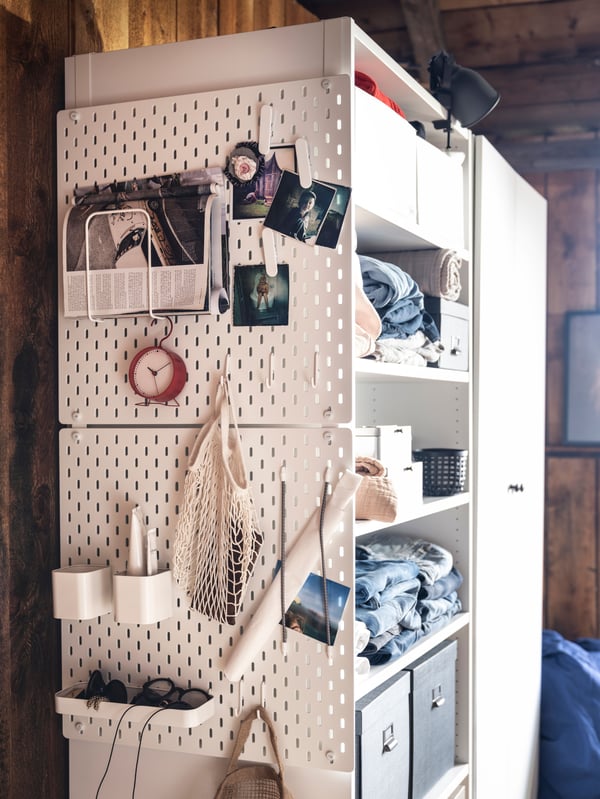 On the side of a large, tall storage unit hang two white SKÅDIS pegboards, holding photographs, trinkets and accessories.