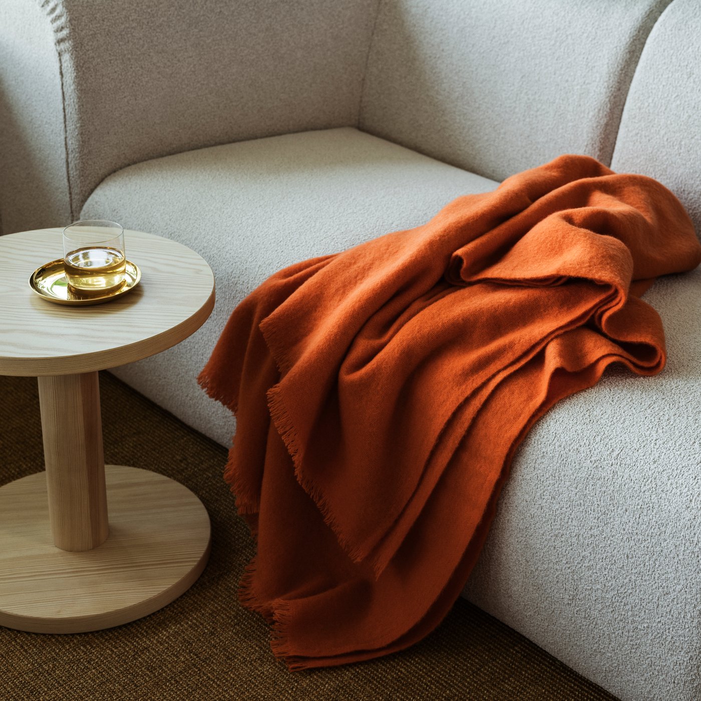 An orange STOCKHOLM throw on a beige sofa next to a wooden side table in the living room.