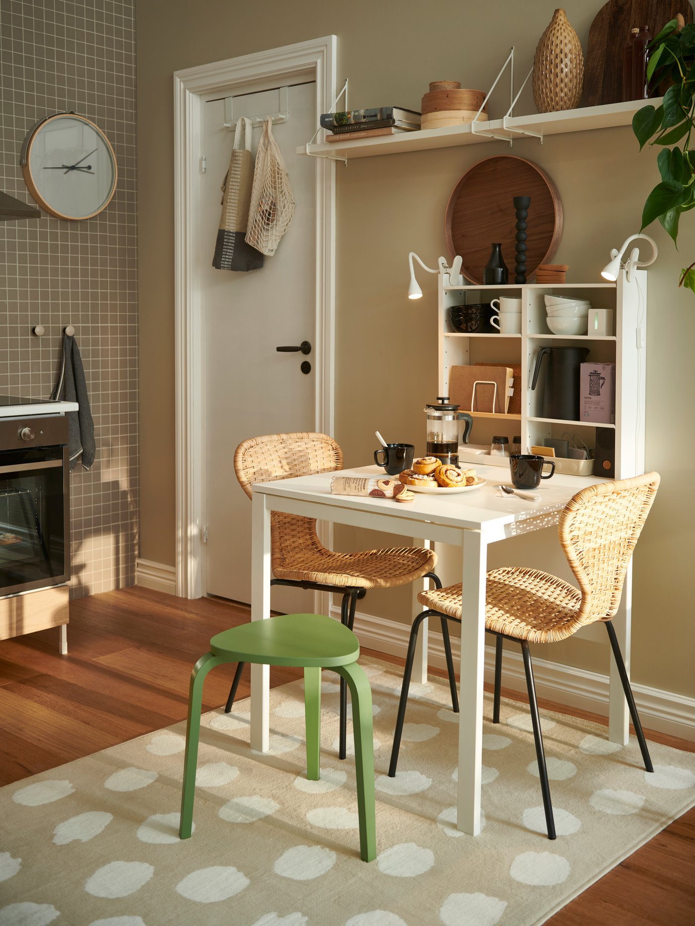 A dining area with a small 2-seater dining table with a white BERGSHULT shelf on the wall.