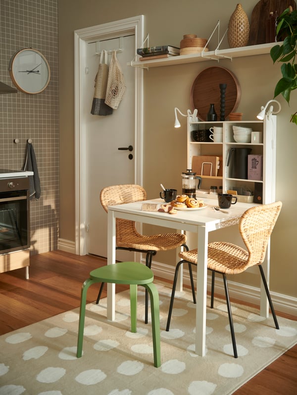 A light kitchen with ÄLVSTA rattan-seat-and-black-frame chairs around a white MELLTORP table, all placed on a BOGENSE rug.