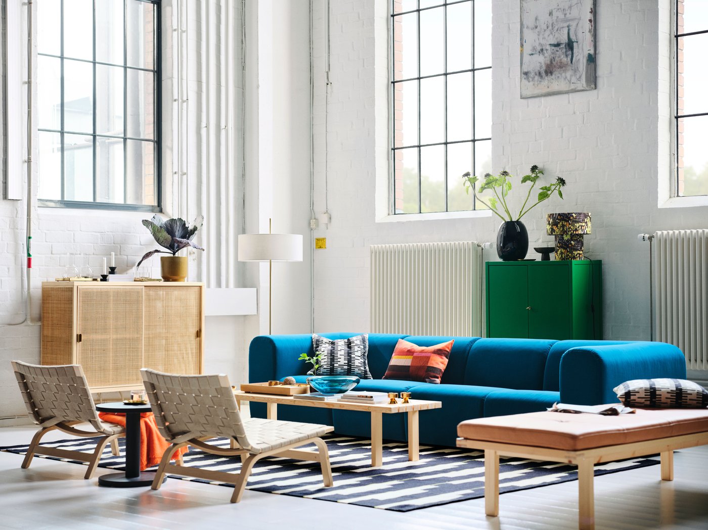 Es ist ein Wohnzimmer mit einem STOCKHOLM 2025 4er-Sofa in Dunkeltürkis, Sesseln und einer Standleuchte zu sehen, die alle um einen Couchtisch angeordnet sind.