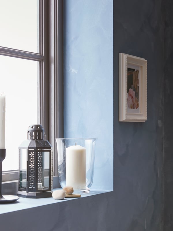 Lanterns and candles sit  in a window.  A large POMP vase can be seen. A